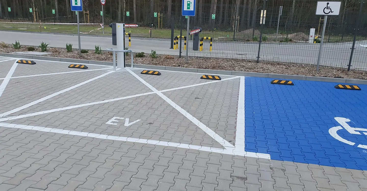 Biała koperta EV i niebieskie miejsce dla osób z niepełnosprawnościami na parkingu z kostki brukowej