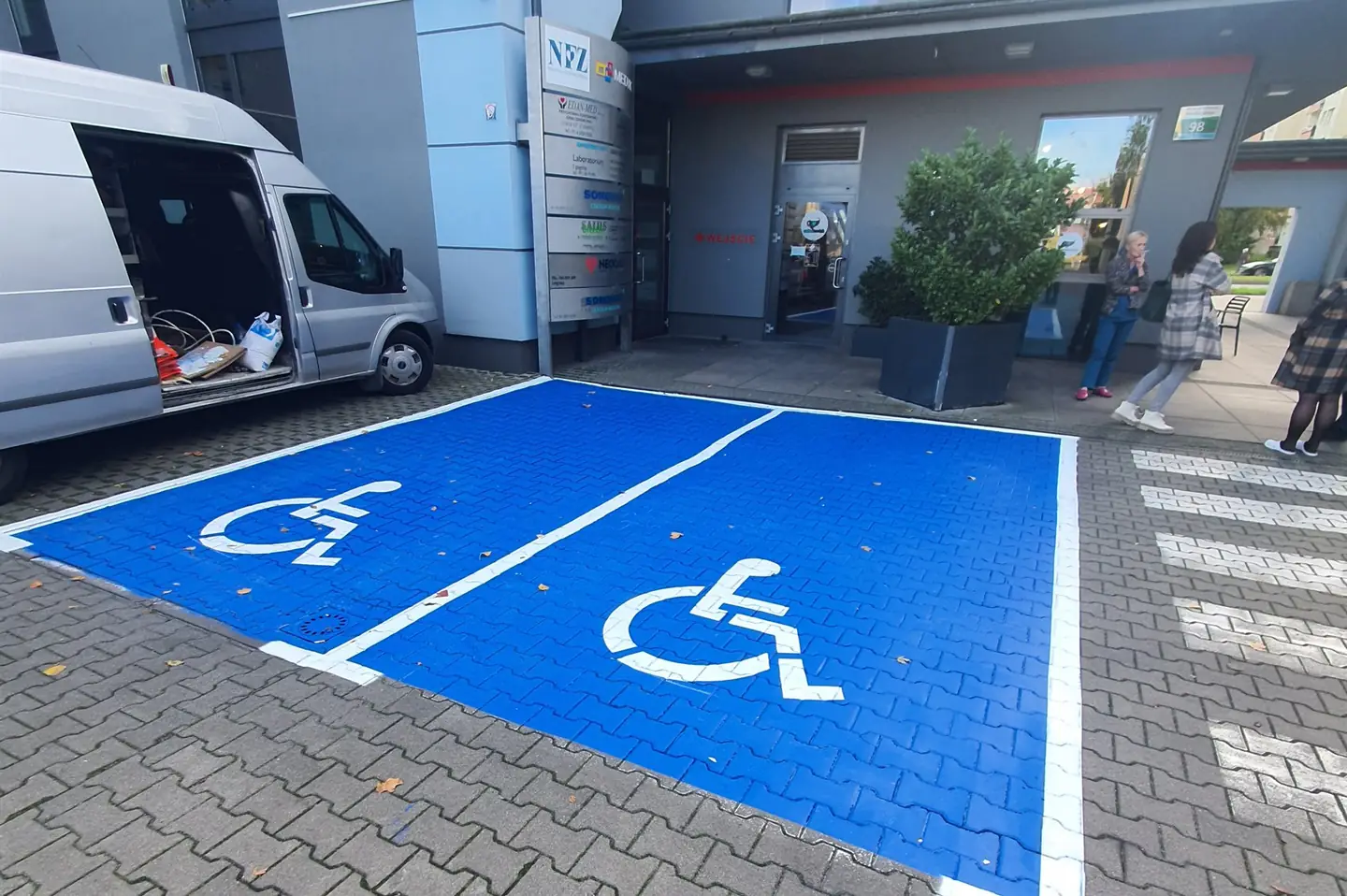 Dwa niebieskie miejsca parkingowe dla osób z niepełnosprawnościami wymalowane przed budynkiem