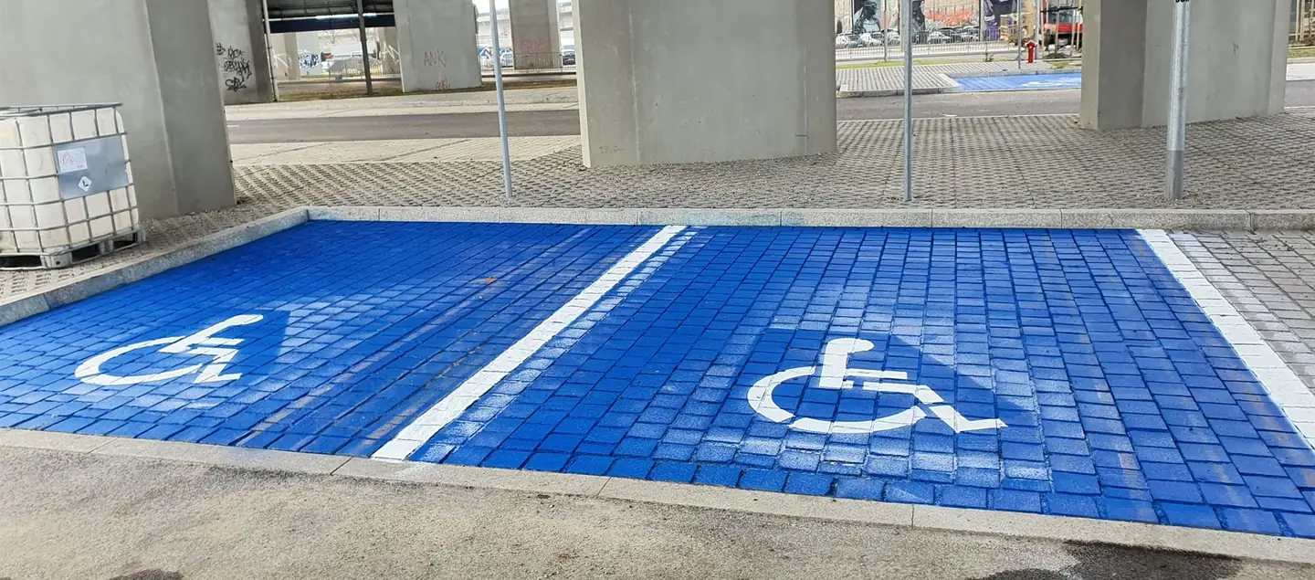 Niebieskie miejsca postojowe z symbolem wózka wymalowane na kostce pod wiaduktem